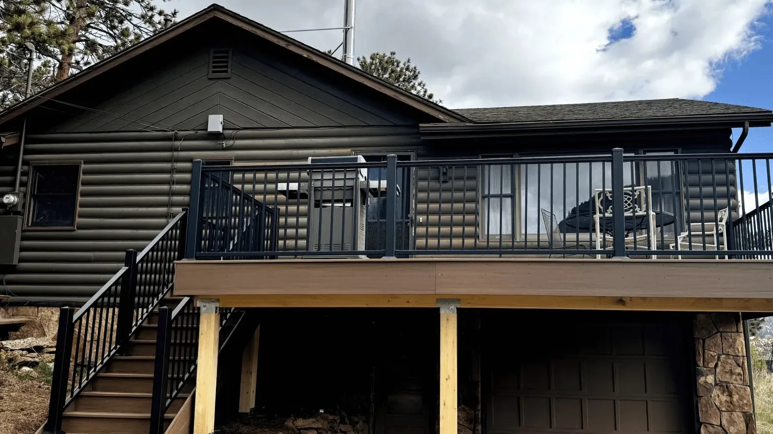 Upper-level vs. ground-level deck example: elevated composite deck with black railing and stairs on a Colorado log home