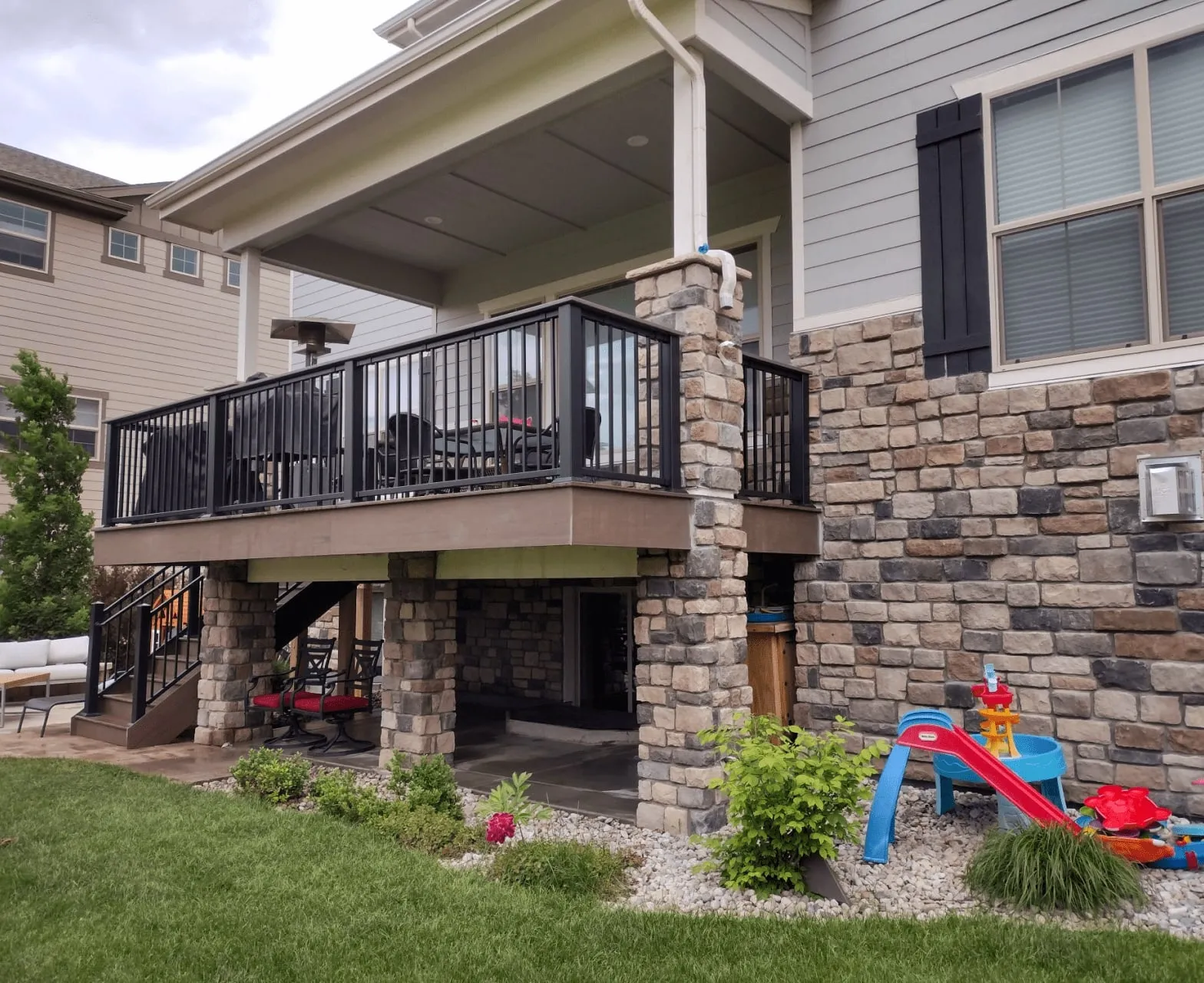 Upper-Level Deck with Usable Space Below Upper-level composite deck with black railing and stone columns, with a patio and play area in the space below