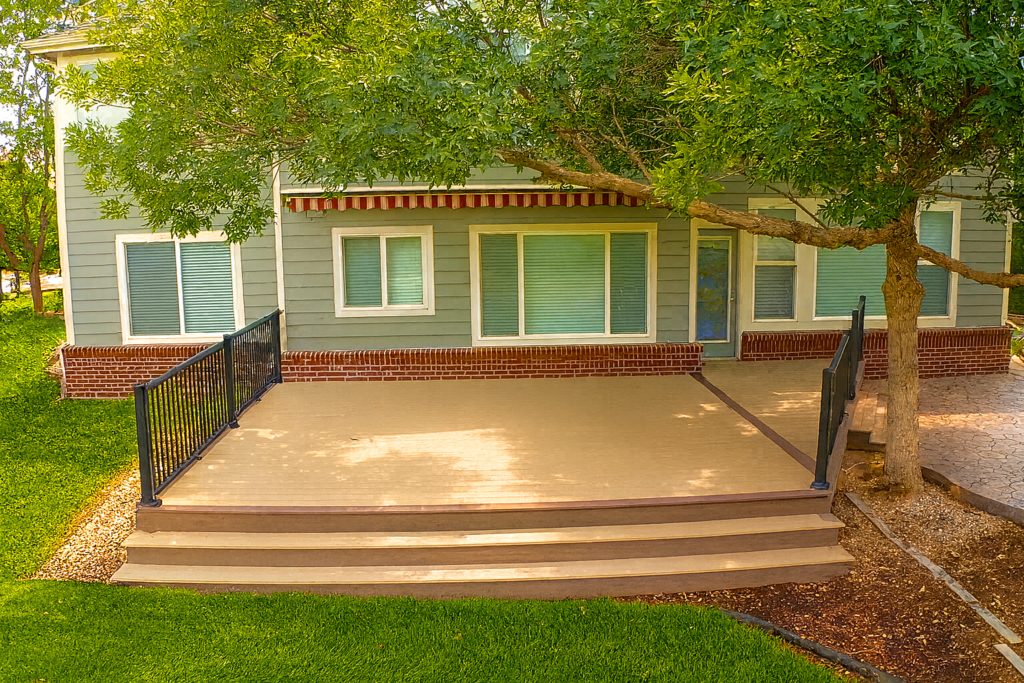 A spacious fireproof deck in a Colorado backyard, featuring composite decking, black metal railing, and built-in steps under mature shade trees.